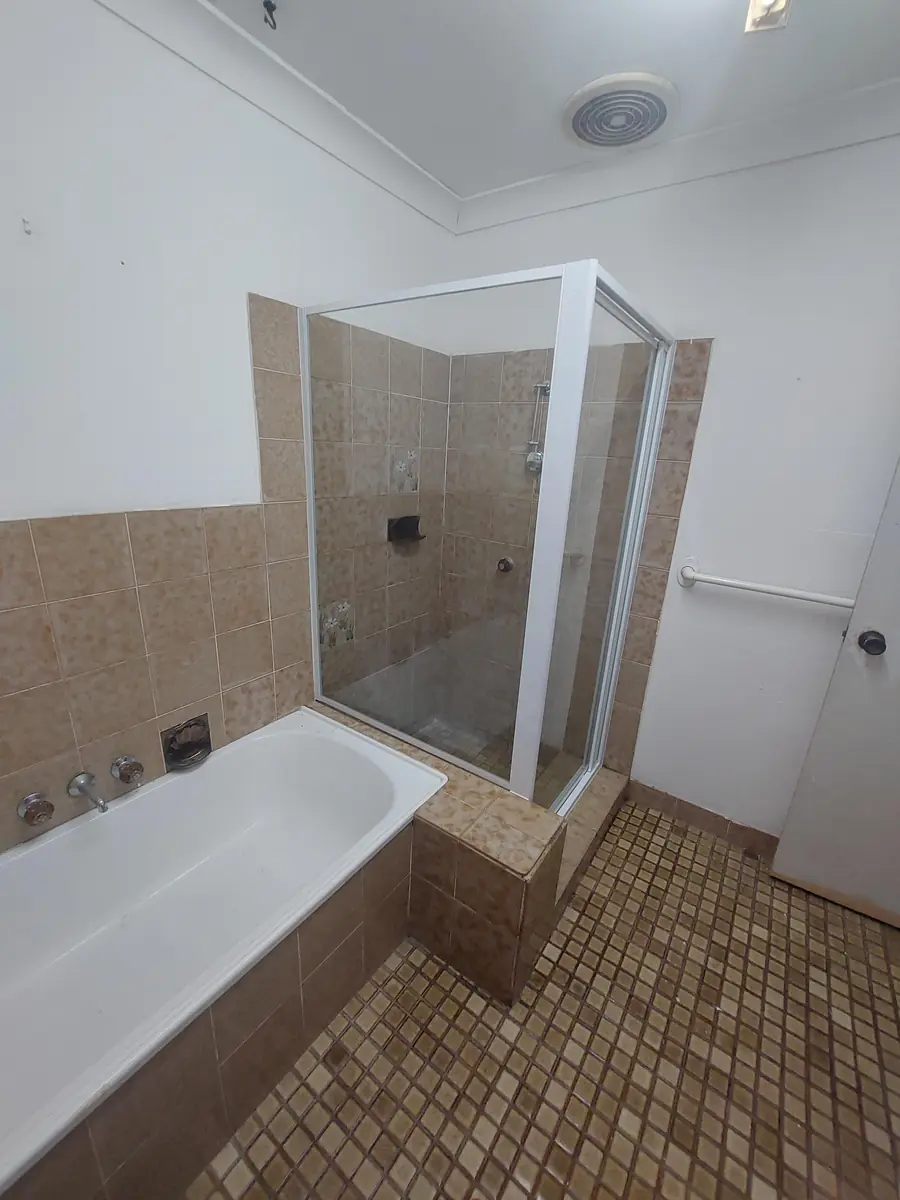 New frameless glass shower screen installed over a tiled bath in a renovated bathroom