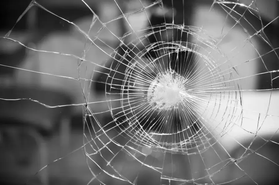 Close-up of a spider-web crack radiating across a broken glass pane